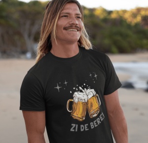 Bărbat cu părul lung blond și mustață, zâmbind și purtând un tricou negru pe care este imprimată o grafică cu două halbe de bere care se ciocnesc, cu spumă revărsându-se și câteva stele sclipitoare deasupra lor. Sub imagine, textul 'Zi de Bere!' este scri