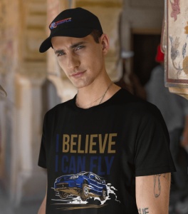 Bărbat purtând un tricou negru cu designul unei mașini sport albastre în zbor și textul 'I BELIEVE I CAN FLY' în albastru și auriu, alături de o șapcă neagră inscripționată cu logo-ul 'Imbracaminte Simplă', pozând într-un cadru urban.