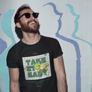 Bărbat zâmbitor cu barbă și ochelari de soare, purtând un tricou negru cu mesajul 'Take it Easy' și o grafică cu o broască țestoasă