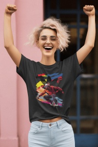 Femeie zâmbitoare cu păr blond și creț, purtând un tricou negru cu un design grafic colorat ce prezintă un skater pe un fundal creativ, ridicând brațele în aer într-o poziție de celebrare, în fața unui perete roz.