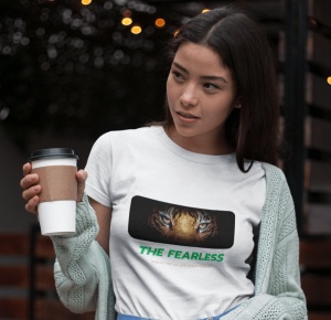 Fată purtând un tricou alb cu un design grafic ce prezintă ochii unui tigru și textul 'THE FEARLESS', ținând o cană de cafea și purtând un cardigan, într-un mediu exterior iluminat.