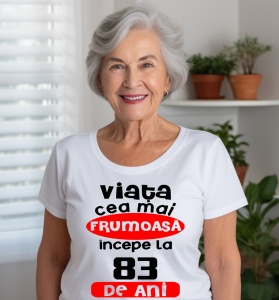 Femeie care poartă un tricou alb personalizat cu mesajul: ''Viata cea mai frumoasa incepe la 83 de ani''.