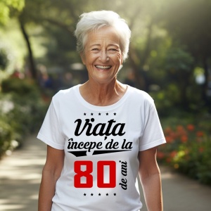O femeie purtând un tricou alb cu textul  'Viața începe de la 80 de ani'. Fundal din lemn cu diferite nuanțe de maro și verde.