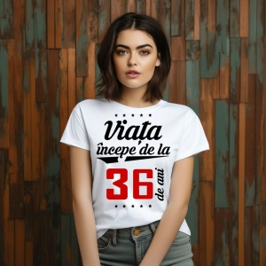 O femeie purtând un tricou alb cu textul  'Viața începe de la 36 de ani'. Fundal din lemn cu diferite nuanțe de maro și verde.
