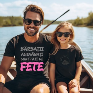 Un tată și fiica sa, zâmbind, sunt așezați într-o barcă pe un lac. Tatăl poartă un tricou negru cu textul "Bărbații adevărați sunt tați de fete", cu "fete" evidențiat în roz, iar fiica sa poartă un tricou negru simplu. Ambii poartă ochelari de soare, iar 