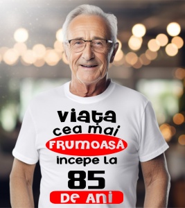 Un bărbat purtând un tricou alb cu textul ''Viața cea mai frumoasă începe la 85 de ani''.
