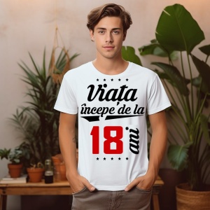 Bărbat tânăr purtând un tricou alb cu mesajul 'Viața începe de la 18 ani', stând într-un mediu decorat cu plante.