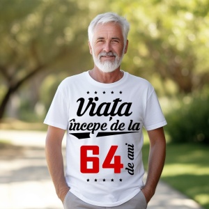 Bărbat în vârstă cu barbă albă, zâmbitor, purtând un tricou alb cu mesajul 'Viața începe de la 64 de ani', stând într-un parc luminat de soare.