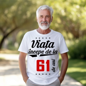 Bărbat în vârstă cu barbă albă, zâmbitor, purtând un tricou alb cu mesajul 'Viața începe de la 61 de ani', stând într-un parc luminat de soare.