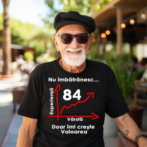 Un bărbat în vârstă, purtând ochelari de soare și o beretă neagră, zâmbind și îmbrăcat într-un tricou negru cu mesajul: „Nu îmbătrânesc... Doar îmi crește valoarea” și un grafic care indică vârsta de 84 de ani pe axa vârstei și experienței. Bărbatul se af