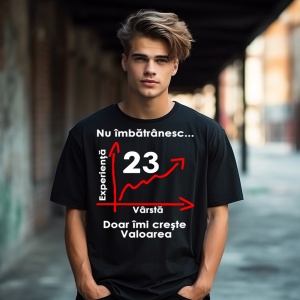 Un tânăr purtând un tricou negru cu mesajul: „Nu îmbătrânesc... Doar îmi crește valoarea” și un grafic care indică vârsta de 23 de ani pe axa vârstei și experienței. Tânărul se află într-un cadru urban, sub o pasarelă, cu clădiri în fundal.