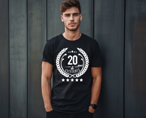 Un bărbat zâmbitor purtând un tricou negru cu textul ''20 de ani de excelență'', înconjurat de o coroană de lauri.