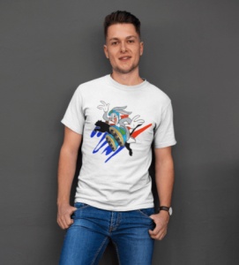 Bărbat zâmbitor purtând un tricou alb cu un design colorat reprezentând un personaj animat într-o scenă dinamică, pozând relaxat într-un cadru interior cu un perete gri în fundal.