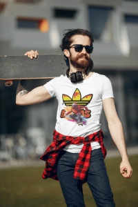 Tânăr cu barbă purtând ochelari de soare, căști la gât și un tricou alb cu un design vibrant ce include un skater și un logo reinterpretat, ținând un skateboard pe umăr, cu o cămașă roșie legată la brâu, pozând într-un cadru exterior urban.