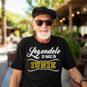 Un bărbat mai în vârstă, purtând ochelari de soare și o beretă neagră, zâmbind și îmbrăcat într-un tricou negru cu mesajul: „Legendele se nasc în Iunie”. Bărbatul se află într-un cadru exterior, pe o terasă, înconjurat de vegetație.