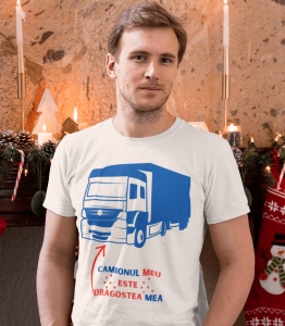 Un bărbat poartă un tricou alb cu o ilustrație albastră a unui camion și mesajul 'Camionul meu este dragostea mea' scris în roșu și albastru. Fundalul este decorat festiv cu lumânări și ornamente de Crăciun.