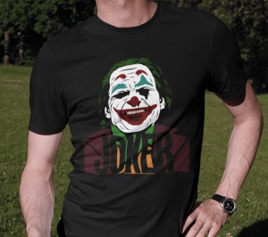Prim-plan al unui bărbat purtând un tricou negru cu un design stilizat al personajului Joker, pe un fundal verde de iarbă. Designul include fața Jokerului zâmbind și textul 'JOKER' în partea de jos.