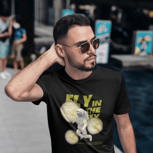 Un bărbat poartă ochelari de soare și un tricou negru cu mesajul 'Fly in the Sky', având o grafică cu un astronaut și planete stilizate. Bărbatul își trece mâna prin păr și este fotografiat într-un cadru urban.
