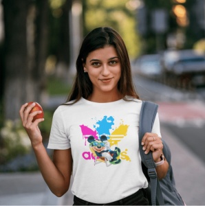 Femeie purtând un tricou alb cu un design colorat ce include logo-ul 'Adidas' și un personaj stilizat(Mickey Mouse), ținând un măr în mână și având un rucsac pe umăr, pozând afară pe o stradă într-un mediu urban.