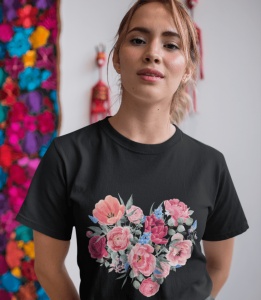 Fată purtând un tricou negru cu un design floral colorat în formă de inimă, într-un cadru interior decorat cu elemente tradiționale viu colorate.