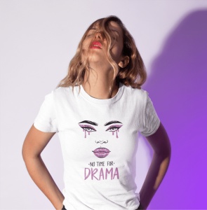 Fată purtând un tricou alb cu un design grafic ce afișează un portret stilizat de femeie cu machiaj dramatic și textul 'No time for drama', pozând într-un cadru iluminat cu tonuri roz și violet.