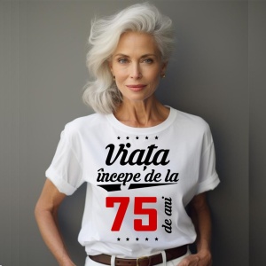 O femeie purtând un tricou alb cu textul  'Viața începe de la 75 de ani'. Fundal din lemn cu diferite nuanțe de maro și verde.