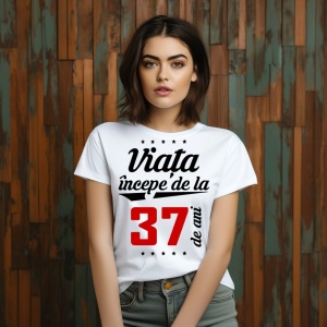 O femeie purtând un tricou alb cu textul  'Viața începe de la 37 de ani'. Fundal din lemn cu diferite nuanțe de maro și verde.