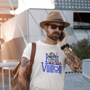 Bărbat purtând o pălărie și ochelari de soare, cu un tricou alb pe care este imprimat un personaj animat albastru(Stitch) și un logo stilizat Louis Vuitton, vorbind la telefon și având un rucsac maro pe umăr și tatuaje pe braț.