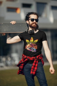 Tânăr cu barbă purtând ochelari de soare, căști la gât și un tricou negru cu un design vibrant ce include un skater și un logo reinterpretat, ținând un skateboard pe umăr, cu o cămașă roșie legată la brâu, pozând într-un cadru exterior urban.