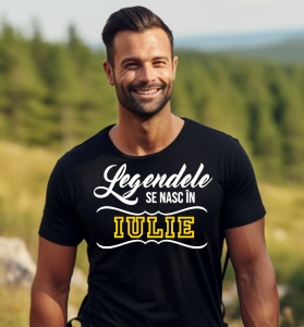 Un bărbat zâmbitor, cu păr scurt și barbă, purtând un tricou negru cu mesajul: „Legendele se nasc în Iulie”. Bărbatul se află într-un cadru natural, cu un peisaj verde în fundal.