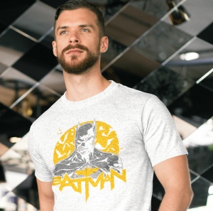 Bărbat purtând un tricou alb cu un design al personajului Batman, având un fundal galben cu lilieci și textul 'BATMAN' dedesubt. Fundalul este un decor modern cu oglinzi și linii diagonale.