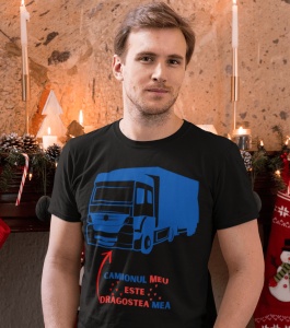 Un bărbat poartă un tricou negru cu o ilustrație albastră a unui camion și mesajul 'Camionul meu este dragostea mea' scris în roșu și albastru. Fundalul este decorat festiv cu lumânări și ornamente de Crăciun.