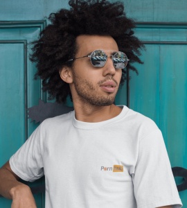 Un tânăr cu păr creț, purtând ochelari de soare și un tricou alb cu un design inspirat de logo-ul 'Pornhub', stă în fața unei uși de lemn de culoare turcoaz. Reflexiile din ochelari arată o scenă urbană, iar el privește într-o parte, adoptând o atitudine 