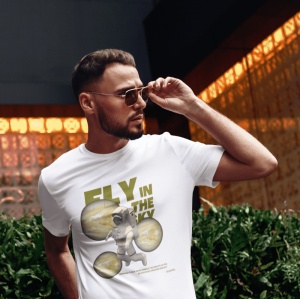 Un bărbat poartă ochelari de soare și un tricou alb cu mesajul 'Fly in the Sky', ilustrat cu un astronaut și imagini stilizate ale planetelor. Bărbatul își ajustează ochelarii într-un mediu urban cu lumini portocalii reflectate în fundal.