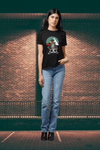 Femeie purtând un tricou negru cu un design inspirat de cultura hip-hop, ce prezintă un personaj cu o bandană și un radio boombox, pe un fundal colorat, pozând în fața unui perete de cărămidă, purtând blugi și pantofi cu toc.