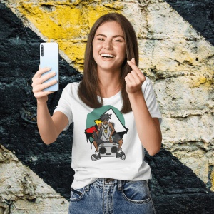 Femeie zâmbitoare purtând un tricou alb cu un design inspirat de cultura hip-hop, ce prezintă un personaj cu o bandană și un radio boombox, pe un fundal colorat, făcând un selfie și gesticulând în fața unui perete colorat.