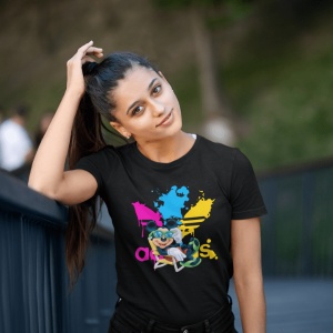 Femeie purtând un tricou negru cu un design colorat ce include logo-ul 'Adidas' și un personaj stilizat(Mickey Mouse), stând afară și ținându-se cu o mână de părul prins în coadă de cal, cu o expresie relaxată.