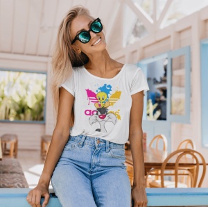 Femeie zâmbitoare purtând ochelari de soare și un tricou alb cu un design colorat cu personajele Tweety și Sylvester din desene animate, relaxându-se într-un spațiu luminos și aerisit cu mobilier din lemn.