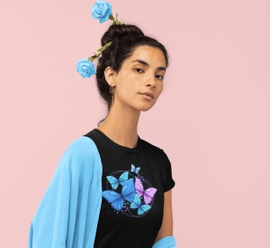 Fată purtând un tricou negru cu un design grafic de fluturi albastri și mov, cu un șal albastru pe umeri și trandafiri albastri în păr, pe un fundal roz.