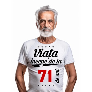 Bărbat în vârstă cu barbă albă, purtând un tricou alb cu mesajul 'Viața începe de la 71 de ani', pe un fundal alb simplu.