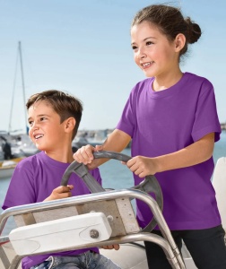 Fată și băiat purtând tricouri violet, zâmbind și bucurându-se de conducerea unei bărci într-un port, cu apă și bărci ancorate în fundal