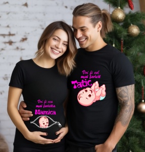 Un cuplu zâmbitor purtând tricouri negre personalizate pentru viitori părinți. Tricoul bărbatului are mesajul 'Voi fi cel mai fericit Tătic' cu un design de bebeluș zâmbitor, iar tricoul femeii are mesajul 'Voi fi cea mai fericită Mămică' cu un design de 
