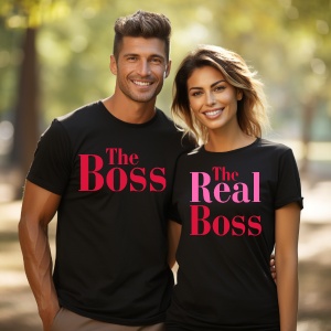 Un cuplu zâmbitor purtând tricouri negre personalizate. Tricoul bărbatului afișează textul 'The Boss', iar tricoul femeii are mesajul 'The Real Boss'. Cuplul pozează într-un cadru natural, în lumină caldă de toamnă.