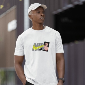 Tânăr afro-american purtând o șapcă albă și un tricou alb cu un design Nike stilizat, care include un personaj animat desenat lângă logo(Catwoman). Fundal urban ușor neclar.