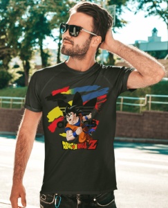 Bărbat purtând ochelari de soare și un tricou negru cu un design colorat ce include un personaj din Dragon Ball Z și un fundal abstract vibrant, pozând într-un cadru exterior, lângă spații verzi.