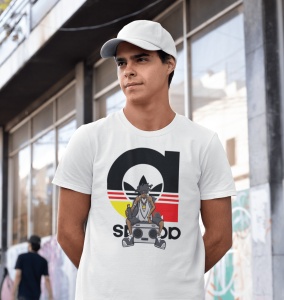 Bărbat purtând o șapcă albă și un tricou alb cu un design ce include un personaj urban cu o boxă portabilă și un logo reinterpretat cu linii galben-roșii și text, pozând pe o stradă urbană cu graffiti pe perete.