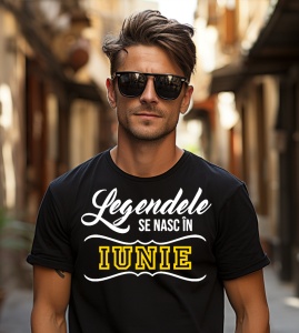 Un tânăr cu părul aranjat și ochelari de soare, purtând un tricou negru cu mesajul: „Legendele se nasc în Iunie”. Bărbatul stă pe o stradă îngustă într-un cadru urban.