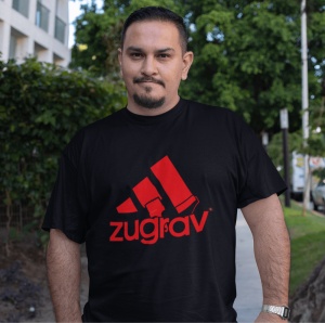 Un bărbat poartă un tricou negru cu un design amuzant inspirat de un logo faimos, înfățișând trei dungi stilizate ca pensule de zugrăvit și textul 'zugrav' scris dedesubt. Fundalul include un spațiu verde și o clădire.