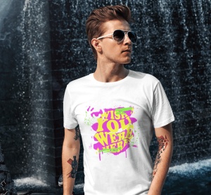 Un bărbat poartă ochelari de soare și un tricou alb cu textul colorat 'Wish You Were Here' scris în culori neon, galben și roz, cu un fundal de stropi verzi și roz, împreună cu o față zâmbitoare alb-negru în colțul stâng sus. În fundal, un perete de apă c