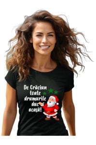 Femeie zâmbitoare purtând un tricou negru cu un design ce îl ilustrează pe Moș Crăciun alături de textul 'De Crăciun toate drumurile duc acasă!' și trei stele verzi.